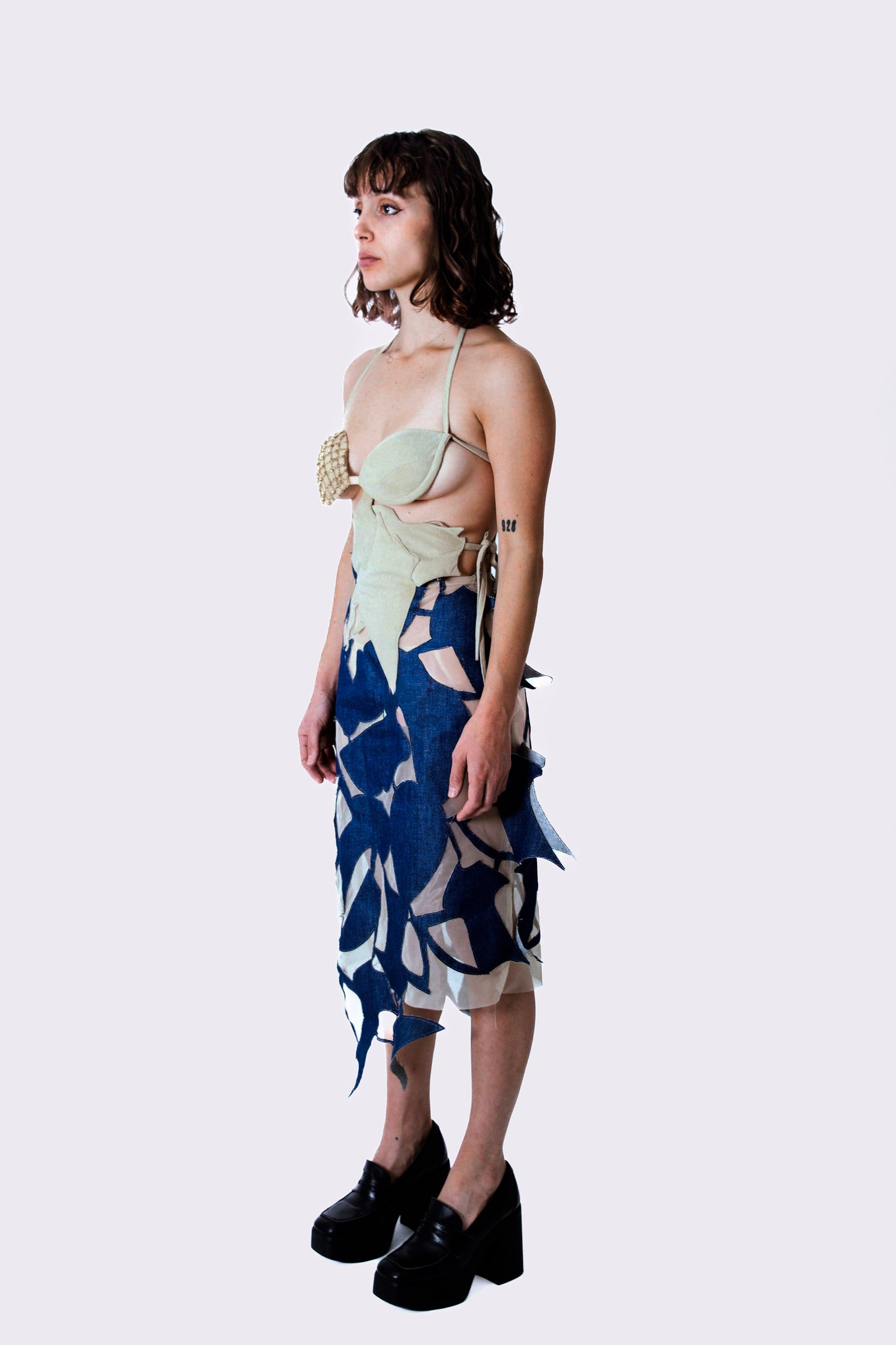 Woman wearing a beige crystal top and blue patterned denim skirt on a white background
